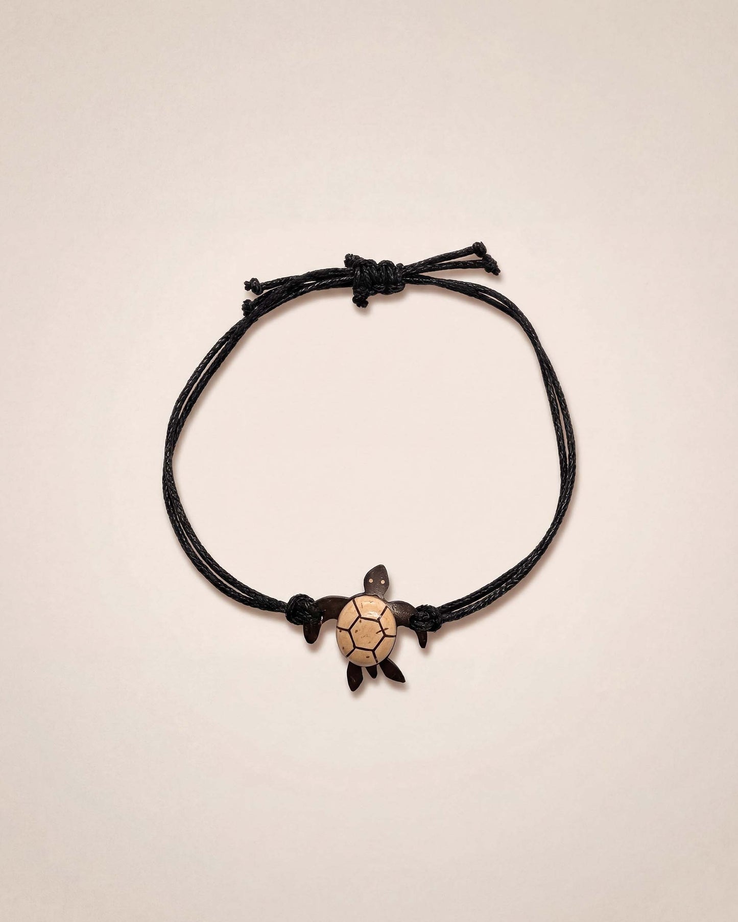 Black cord bracelet with a turtle charm on a beige background
