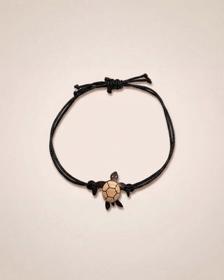 Black cord bracelet with a turtle charm on a beige background