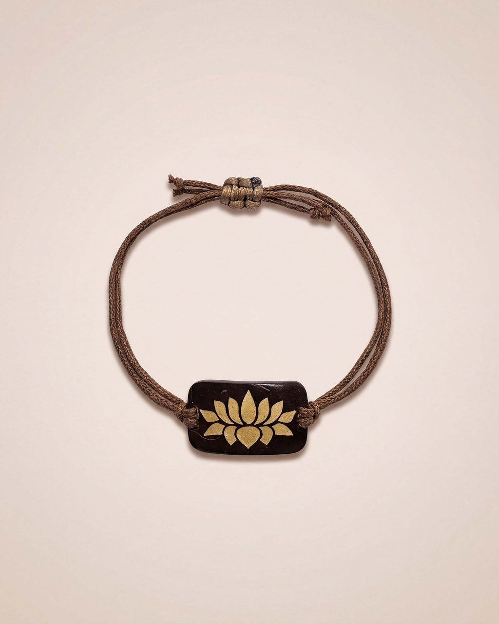 Bracelet with a brown cord and gold emblem on a beige background