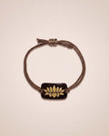 Bracelet with a brown cord and gold emblem on a beige background