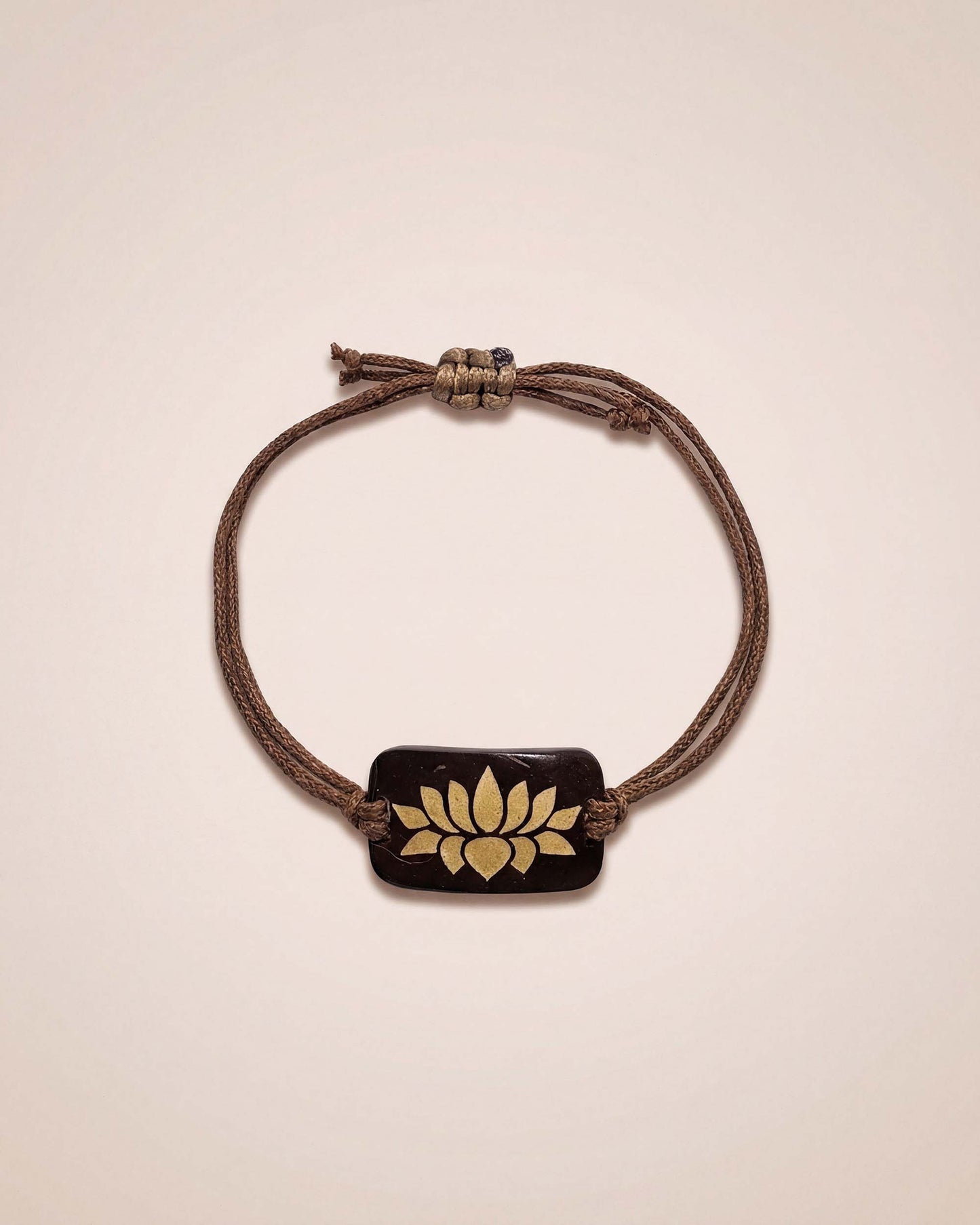 Bracelet with a brown cord and gold emblem on a beige background
