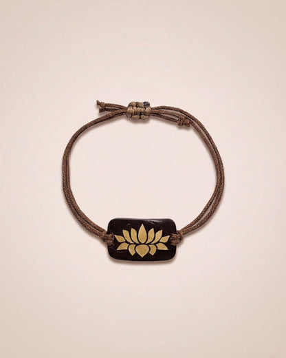 Bracelet with a brown cord and gold emblem on a beige background