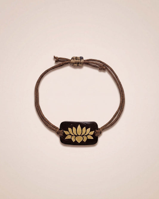 Bracelet with a brown cord and gold emblem on a beige background